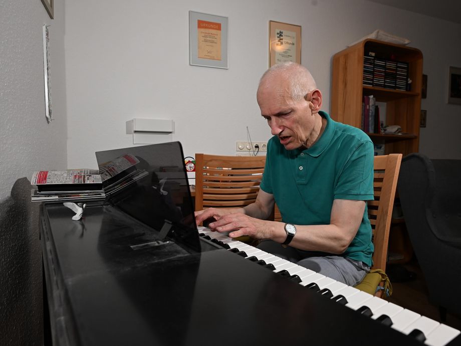 Christoph Maillard, ein älterer Mann im grünen Hemd, sitzt am Klavier und spielt.
